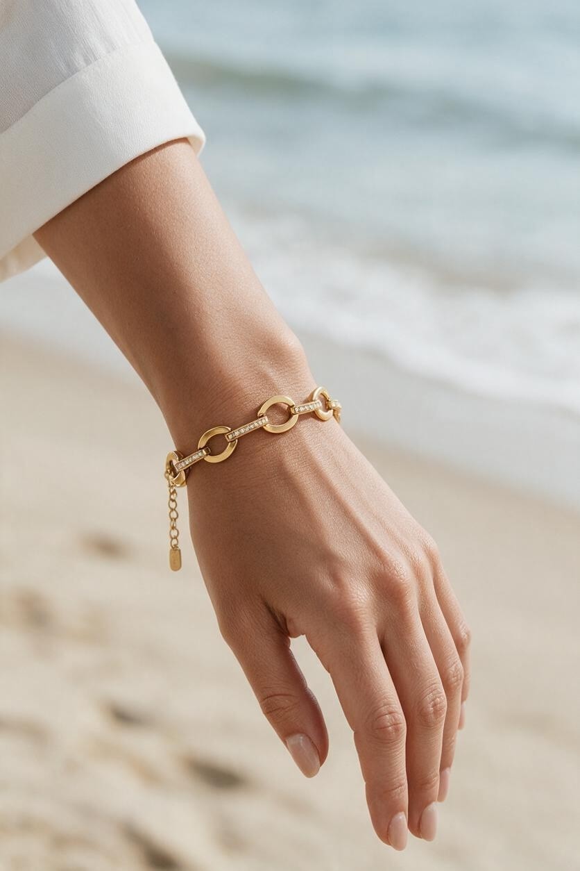 Calilo Australia gold chain link bracelet with crystal accents worn on a wrist against a blurred beach background.
