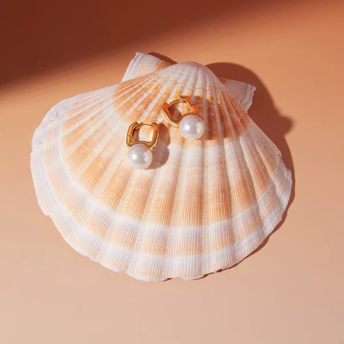 Pearl earrings on a seashell with a peach background