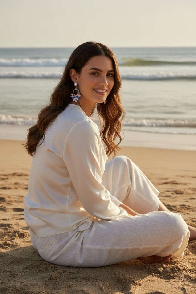 A woman wearing Calilo Australia Adele statement drop earrings with multi-faceted lilac and blue crystals on the beach