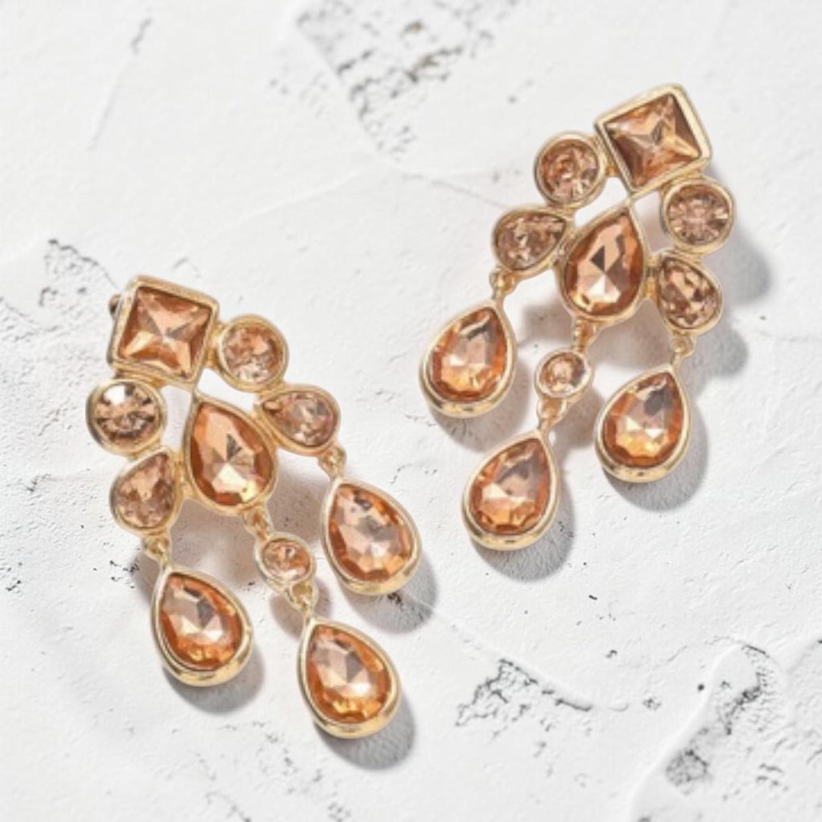 Calilo Australia gold-tone chandelier earrings with cascading faceted teardrop crystals on a textured white surface.
