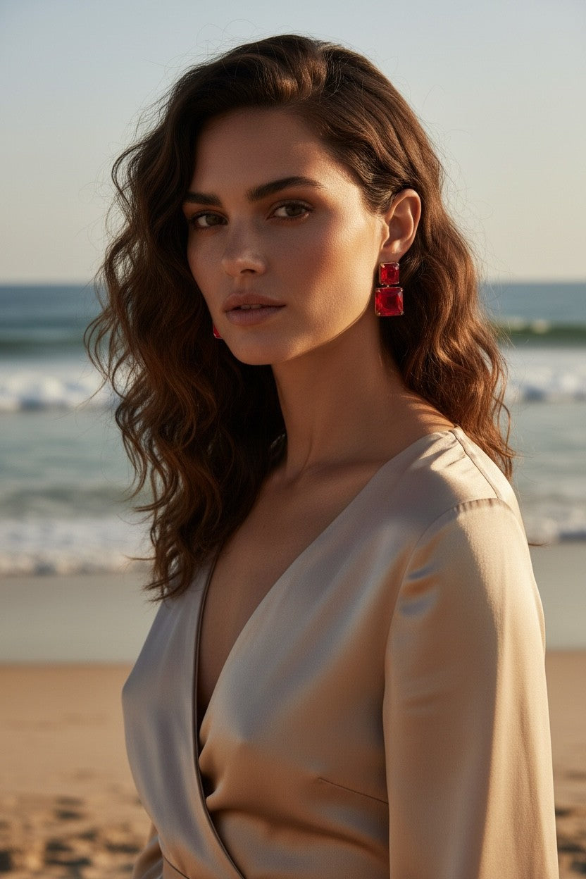 A woman wearing Calilo Australia double-drop square earrings with vibrant red faceted stones and gold-tone settings.